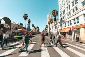 An action-shot of a group of casual people walking across the street in Los Angeles during the daytime. 