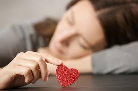 Woman pondering while holding a heart symbol. 