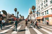 An action-shot of a group of casual people walking across the street in Los Angeles during the daytime. 